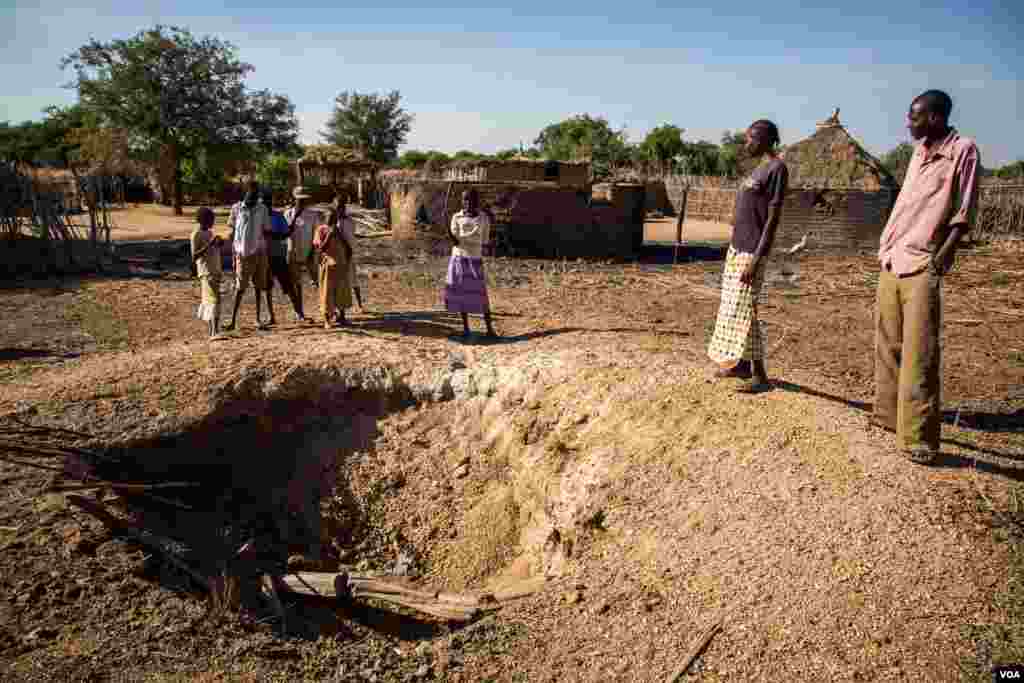 Omar Jajani and his family stand around a bomb crater made by an Antonov bomber. He says the bombing destroyed the whole compound where his home once was, everything is gone. (Adam Bailes/VOA News)