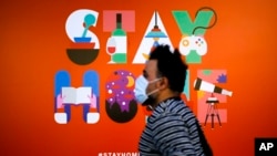 បុរស​ម្នាក់​ដែល​ពាក់​ម៉ាស់​ដើរ​ពី​មុខ​ផ្ទាំង​បដា​មួយ​ដែល​ណែនាំ​ឱ្យ​មនុស្ស​ស្នាក់​នៅ​ផ្ទះ នៅ​ហាង​ទំនិញ​មួយ​នៅ​ក្នុង​ក្រុង​បែរឡាំង ប្រទេស​អាល្លឺម៉ង់ កាលពី​ថ្ងៃទី២០ ខែមេសា ឆ្នាំ២០២០។