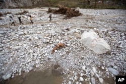 Residents walk past a body, a Hurricane Matthew victim, along the Bois Droit river, in Port-a-Piment, a district of Les Cayes, Haiti, Oct. 18, 2016.