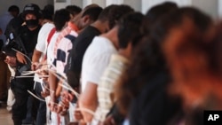 FILE - A policeman of an anti-gang unit stands next to handcuffed alleged members of the Mara Salvatrucha (MS-13) detained during a police raid in San Salvador, El Salvador, Jan. 31, 2014.