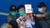 Pro-democracy activist Avery Ng, center, holds a book with a cover picture of Chinese President Xi Jinping as he is escorted by Correctional Services officers to a prison van for a court in Hong Kong, May 28, 2021. 