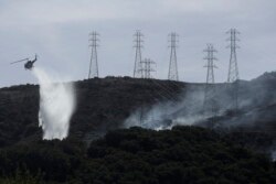 FILE - A helicopter drops water near power lines and electrical towers while working at a fire on San Bruno Mountain near Brisbane, California, Oct. 10, 2019.
