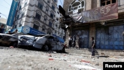 Orang-orang berdiri di samping mobil-mobil yang hancur pasca bentrokan pejuang Houthi dengan pasukan yang setia kepada mantan presiden Yaman Ali Abdullah Saleh baru-baru ini di Sanaa, Yaman, 5 Desember 2017.