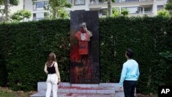 A couple stop to look at a bust of Belgium's King Leopold II, which has been damaged by red paint, graffiti and cement, at a park in Ghent, Belgium, June 19, 2020.
