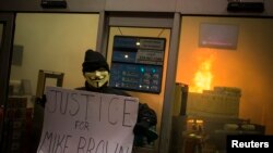 អ្នក​តវ៉ា​​ម្នាក់​លើក​ផ្ទាំង​សញ្ញា​ខាង​ក្រៅ​ហាង​លក់​ថ្នាំ​ពេទ្យ​ដែល​កំពុង​ឆេះ​ ក្រោយ​ក្រុម​គណៈវិនិច្ឆ័យ​​​បាន​សម្រេច​ថា​មិន​ធ្វើការ​កាត់ទោស​លើ​ការ​បាញ់​សម្លាប់​យុវជន​ស្បែកខ្មៅ​ឈ្មោះ ​Michael Brown ​ក្នុង​ទីក្រុង Ferguson រដ្ឋ Missouri កាល​ពី ថ្ងៃ​ទី​២៤ ខែ​វិច្ឆិកា ឆ្នាំ​២០១៤។