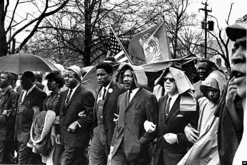 លោក John&nbsp;Lewis (​ស្ដាំបង្អស់) ដើរ​កៀក​ដៃ​ជាមួយនឹង​ក្រុម​មេដឹកនាំ​ទាមទារ​សិទ្ធិ​ពលរដ្ឋ​​ដទៃទៀត ដឹកនាំ​ការ​តវ៉ា​ទាមទារ​សិទ្ធិ​ឲ្យ​ពលរដ្ឋ​ស្បែក​ខ្មៅ ដោយ​ដើរ​ដង្ហែ​ក្បួន​​ទៅ​កាន់​សាលាក្ដី​ក្នុង​ក្រុង Montgomery រដ្ឋ​ Alabama ថ្ងៃទី​១៧ ខែមីនា ឆ្នាំ​១៩៦៥។