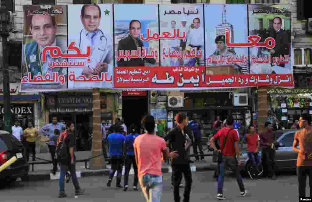 People walk under campaign posters of presidential candidate and former army chief Abdel Fattah al-Sissi a day ahead of presidential elections in Cairo, May 25, 2014.
