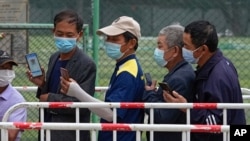Residents wearing face masks look at their smartphones showing a health code as they line up to receive the Sinopharm COVID-19 vaccine at a vaccination center in Central Business District in Beijing on June 2, 2021.