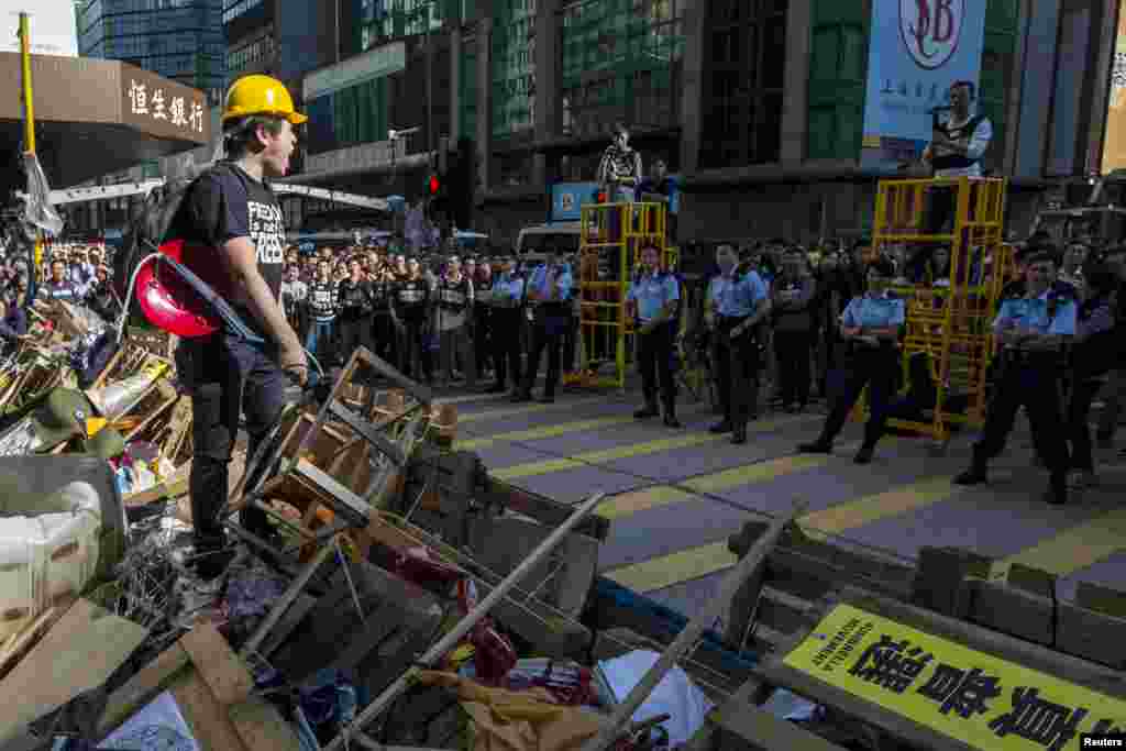 A pro-democracy protester who has climbed atop a barricade shouts at police after the arrival of bailiffs to dismantle the Mong Kok protest site following a court-issued eviction order, in Hong Kong, Nov. 25, 2014.