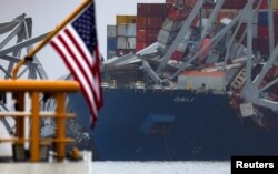 The U.S. flag flies on the stern of a U.S. Coast Guard patrol boat as it passes the wreckage of the Dali cargo vessel, which crashed into the Francis Scott Key Bridge, causing it to collapse, in Baltimore, Maryland, March 27, 2024.
