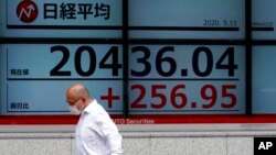 បុរស​ម្នាក់​ពាក់​ម៉ាស់​ដើរ​កាត់​ក្ការ​អេឡិចត្រូនិក​បង្ហាញ​ពី​សន្ទស្សន៍​ទីផ្សារ​ភាគហ៊ុន Nikkei 225 របស់​ជប៉ុន នៅ​ឯ​ក្រុមហ៊ុន​សន្ដិសុខ​មួយ​ក្នុង​ទីក្រុង​តូក្យូ ថ្ងៃ​ទី​១១ ខែឧសភា ឆ្នាំ​២០២០។ 