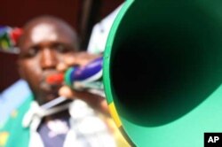Zimbabwean hawker Walter Kanyegoni blows a plastic vuvuzela trumpet he's painted in the colors of the South African flag
