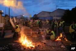 FILE - Demonstrators stand in front of a makeshift barricade set up by the so-called yellow jackets to block the entrance of a fuel depot in Le Mans, western France, Tuesday, Dec. 5, 2018.