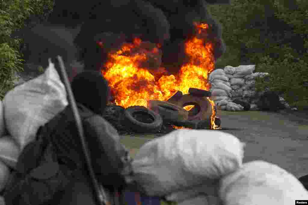 A pro-Russian separatist guards a checkpoint as tyres burn in front of him, near the town of Slaviansk in eastern Ukraine May 2, 2014.