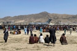 FILE - In this Aug. 16, 2021, file photo, hundreds of people gather near a U.S. Air Force C-17 transport plane at the perimeter of the international airport in Kabul, Afghanistan.