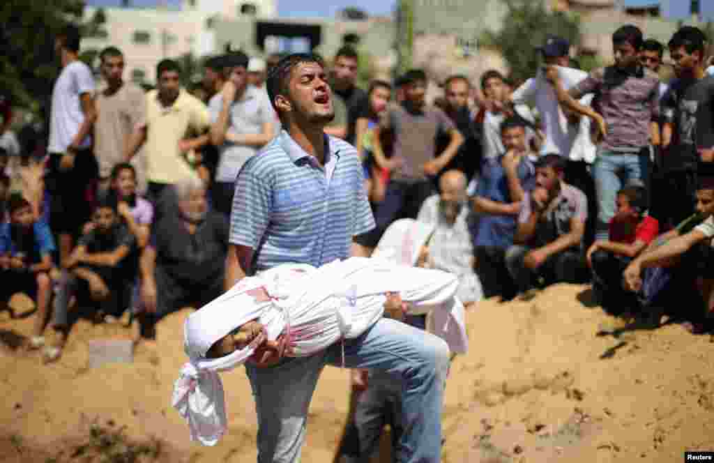A Palestinian man carries the body of a girl from the Abu Nejim family, whom medics said was killed along with other eight family members by an Israeli air strike in the northern Gaza Strip, Aug. 4, 2014.