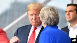 U.S. President Donald Trump, left, clenches a fist when talking to British Prime Minister Theresa May during a summit of heads of state and government at NATO headquarters in Brussels on Wednesday, July 11, 2018. NATO leaders gather in Brussels for a two-day summit to discuss Russia, Iraq and their mission in Afghanistan.