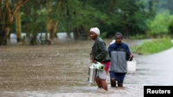 Women wade through flood waters after a seasonal river burst its banks following heavy rainfall in Kitengela municipality of Kajiado County, near Nairobi, Kenya, May 1, 2024. 