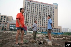 Workers walk near a building with windows shattered by the shockwave from a nearby explosion in northeastern China's Tianjin municipality, Aug. 13, 2015.