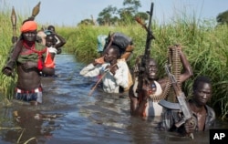 FILE - Rebel soldiers are seen protecting civilians from the Nuer ethnic group as they walk through flooded areas to reach a makeshift U.N. camp for the displaced in the town of Bentiu, South Sudan, Sept. 20, 2014. After two years of civil war, rebel leader Machar and South Sudan President Salva Kiir signed a peace deal in August 2015.