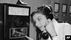 As coins slide down before her eyes, a German woman uses a new long distance dial telephone for public booths, July 17, 1957. (AP Photo)