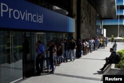 People line up to withdraw cash from an automated teller machine outside a Banco Provincial branch in Caracas, Venezuela, Dec. 12, 2016.
