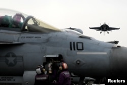 U.S. Navy sailors perform checks on a F-18 fighter jet as another F-18 prepares to land on the USS Harry S. Truman aircraft carrier in the eastern Mediterranean Sea, May 4, 2018.
