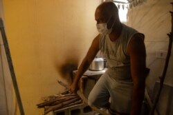 Juarez Viana breaks a stick to fit on the wood stove he has been using to cook for his family since last month, in São Paulo, Nov. 14, 2021. (Yan Boechat/VOA)