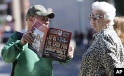 A vendor shows Marie Ross of Pennsylvania a magazine during her visit to Dealey Plaza in Dallas, Oct. 25, 2017.