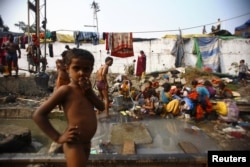 FILE - People living in slums near the railway tracks use the water supply from its broken pipelines to wash clothes and take baths in Delhi, Nov. 13, 2012.