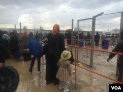 Families wait in the rain for buses to take them to camps or their relatives' homes on April 3, 2017, in Hammam Alil, Iraq. (H. Murdock/VOA)