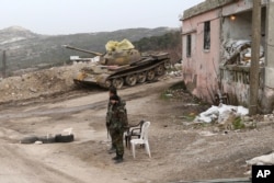 Syrian troops stand, with a destroyed tank in the background, on a street in Salma, Syria, Jan. 22, 2016. Syrian government forces, relying on Russian air cover, have recently seized Salma, located in Syria's province of Latakia, from militants.