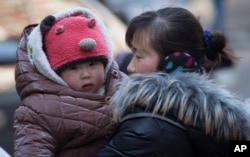 FILE - A Chinese woman cuddles her child in Beijing, China, March 6, 2014. China announced Thursday it was ending its long-standing one-child policy and will now allow all couples to have two children.