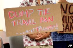 Pengkritik larangan perjalanan Presiden Donald Trump mengangkat poster selama konferensi pers dengan Jaksa Agung Hawaii, Douglas Chin, 30 Juni 2017 di Honolulu.