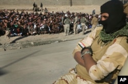 A face covered Iraqi soldier sits on his humvee in front of scores of Iraqi male residents who were rounded up by Iraqi forces, in Gogjali neighborhood, in Mosul, Iraq, Nov. 24, 2016. Iraqi forces urged them to come out with information about the Islamic State.