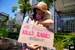 Seorang aktivis membawa plakat dengan menggendong boneka yang digambarkan sebagai bayi yang terkena dampak polusi udara. (Foto: AP)