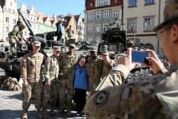 FILE - A woman takes a picture with U.S. soldiers, who are part of a NATO multinational battalion on their way from Germany to Orzysz, northeastern Poland, during a military picnic with NATO troops in Wroclaw, Poland, March 27, 2017.