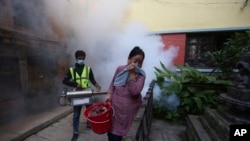 A Nepalese woman covers her face as a worker fumigates an area in an attempt to control mosquito-borne diseases in Kathmandu, Nepal, Sept. 5, 2019. The government says dengue cases has shot up by more than 65% across the country in the last week.