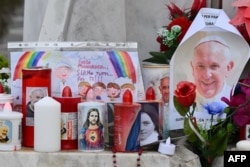 Lilin, bunga, dan potret Paus Fransiskus diletakkan di patung Yohanes Paulus II di luar rumah sakit Gemelli tempat Paus Fransiskus dirawat, di Roma pada 24 Februari 2025. (Foto: AFP)
