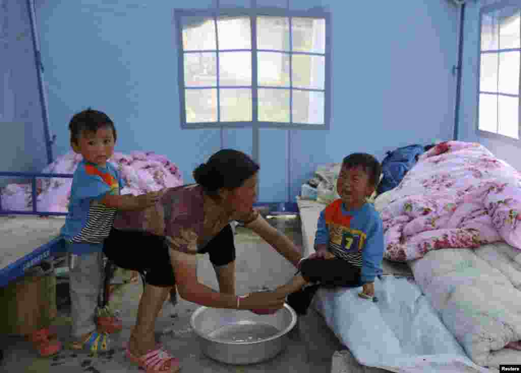 A woman washes the feet for a crying child under a tent at a quake zone at Longtoushan, Dudian county, in Zhaotong, Yunnan province, Aug. 5, 2014.