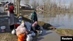 A woman fills drinking water in a container from a municipal water pipe as others wait for their turn on the outskirts of Srinagar, March 22, 2015. World Water Day is observed March 22. 