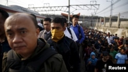 FILE - Indonesia workers walk through train tracks as they go to work at Tanah Abang train station in Jakarta, Oct. 15, 2015. An Indonesian presidential decree requires all employers to provide language training in Bahasa Indonesia to foreign workers. 