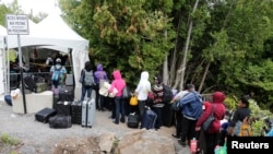 FILE - A line of asylum seekers who said they were from Haiti wait to enter into Canada from Roxham Road in Champlain, New York, Aug. 7, 2017.