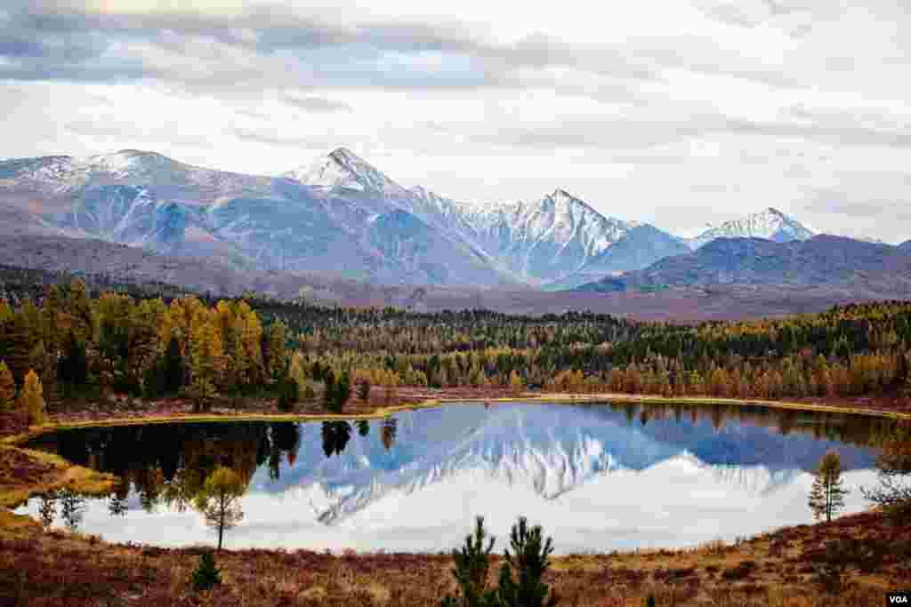On a cool autumn evening, a mountain lake carries the reflections of high mountain slopes where the first snows of winter have already fallen. These high altitudes are home to the snow leopard and its prey, the Argali sheep.