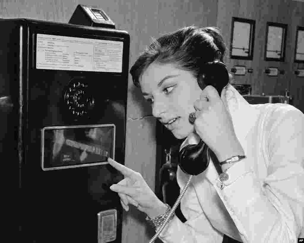 As coins slide down before her eyes, a German woman uses a new long distance dial telephone for public booths, July 17,1957.(AP Photo)