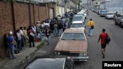 FILE - People line up outside a supermarket next to motorists queuing for gas near a gas station of the Venezuelan state-owned oil company PDVSA in San Cristobal, Venezuela, Nov. 10, 2018. 