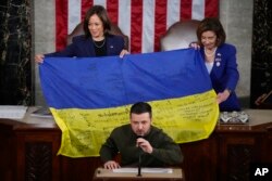Vice President Kamala Harris and House Speaker Nancy Pelosi of Calif., right, react as Ukrainian President Volodymyr Zelenskyy presents lawmakers with a Ukrainian flag autographed by front-line troops in Bakhmut, in Ukraine's contested Donetsk province, as he addresses a joint meeting of Congress on Capitol Hill in Washington, Wednesday, Dec. 21, 2022.