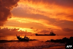 FILE - A fishing boat (L) heads out to sea at dawn in Lhokseumawe, Aceh on August 9, 2021. (Photo by Azwar Ipank / AFP)