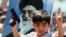 FILE - An Iraqi boy living in Iran holds a toy gun and flashes a victory sign in front of a poster of Iranian supreme leader Ayatollah Ali Khamenei in demonstration against Sunni militants of the Islamic State group in Tehran, June 20, 2014.