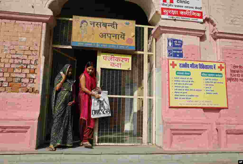 Indian women walk past a billboard advocating sterilization hung at the entrance of the District Women&rsquo;s Hospital in Varanasi, India, Nov. 12, 2014.